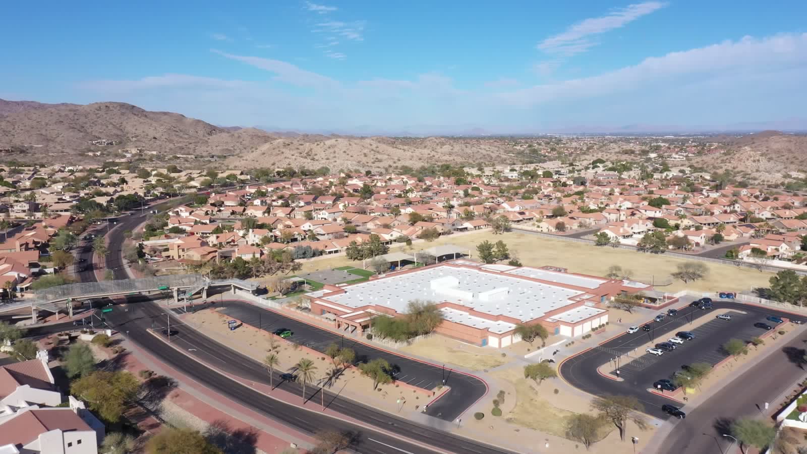 A wide aerial over Ahwatukee rooftops and streets, with the mountains behind