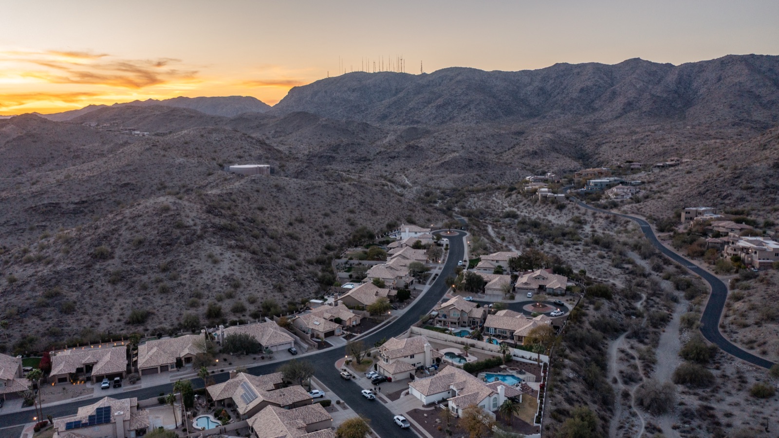 Homes along a curving street at the foot of South Mountain at sunset, with radio towers on the ridge